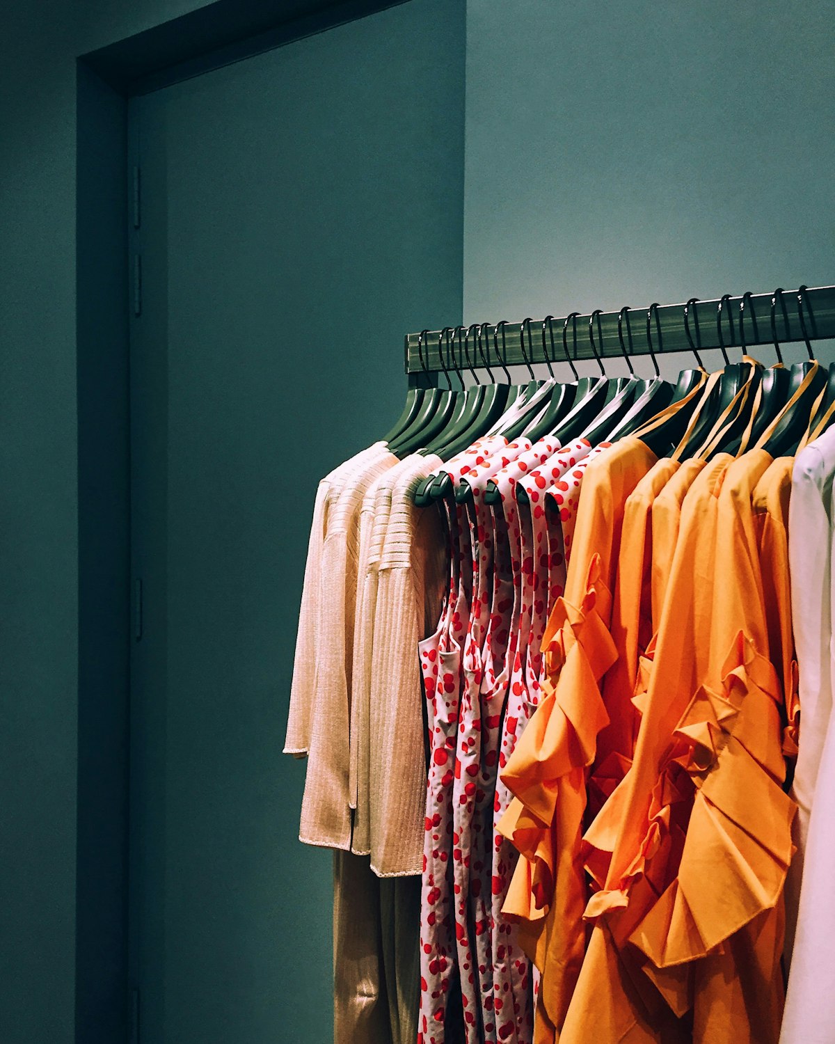 Clothing hanging on a rack against a deep green tiled wall